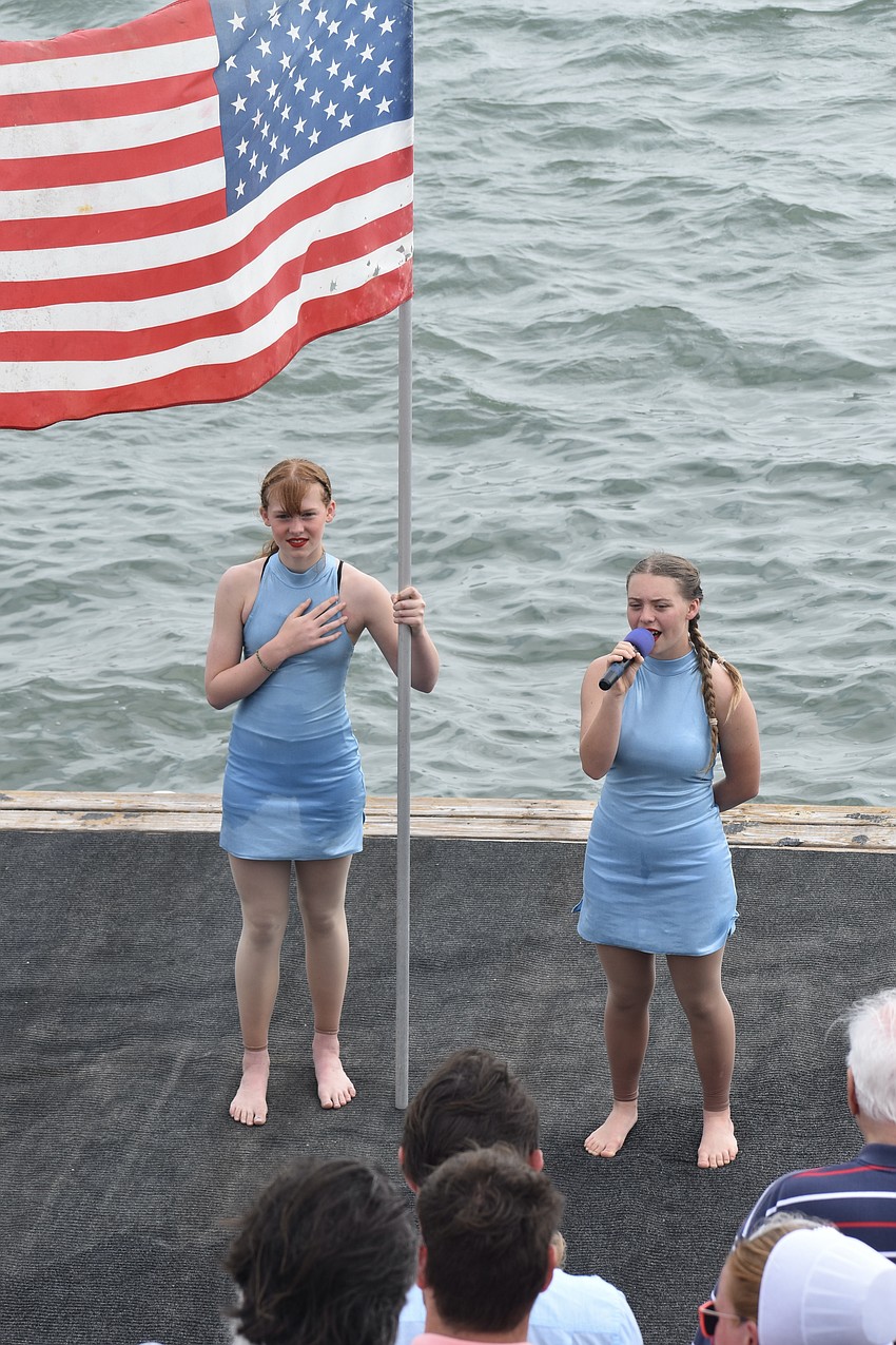 Peyton Robbins, 13, holds the flag, while Lauren Taylor Nock, 15, sings the national anthem.