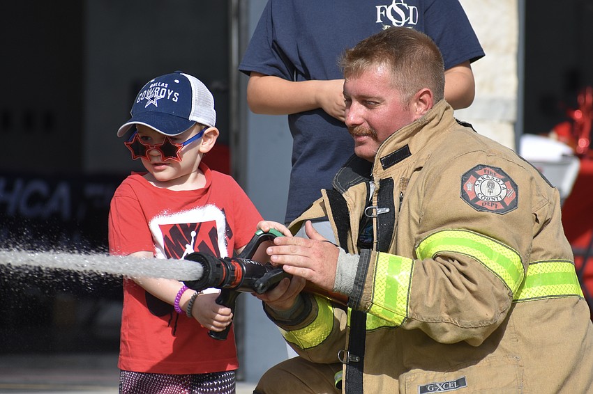 Sarasota's Declan Morrison, 2, tries the fire hose with the help of Firefighter/EMT Marshall Germond.