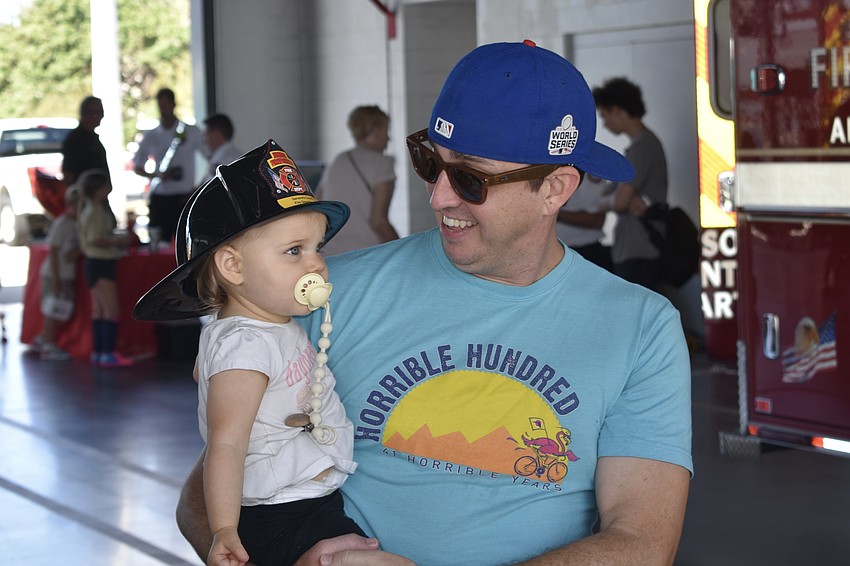 Sarasota's Claire Lambert, 1, tries on a fire helmet with the help of her father Matt Lambert.