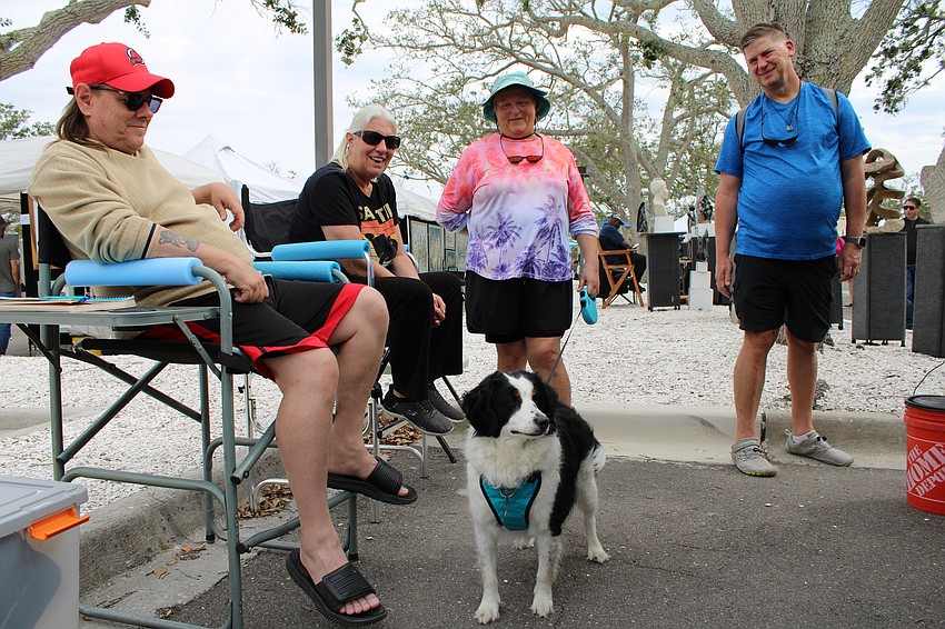 Paula and Lee Smit, joined by Nori the Bernedoodle, chat with Bonnie and Scott Keane beside Bonnie's display of her abstract art.