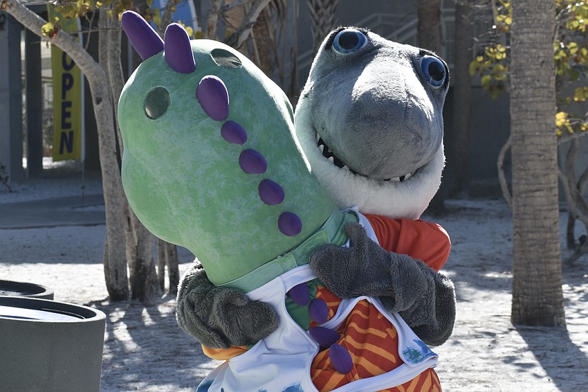 Morris the Explorasaurus of Great Explorations Children's Museum, greets Gilly of Mote Marine Laboratory & Aquarium, with a hug.