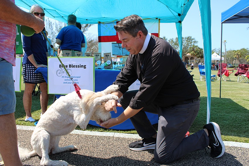 Lily Tonge, a sheepadoodle brought to the open house by owner Stephanie Tonge, bows and accepts a treat while getting a pet blessing from Father David Marshall of All Angels Episcopal Church.