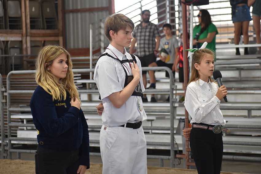 Sarasota High School senior Stormi McMenamin, the Florida Virtual School Future Farmers of America chapter representative, and Andrew Hopper, who was on the senior level in the dairy goat competition, stand by fourth grader Sofia Rose Peric as she sings the national anthem.