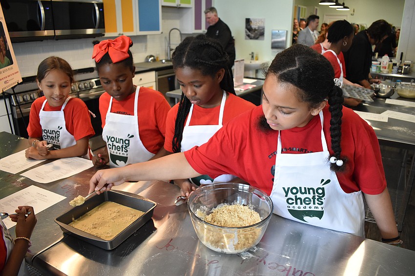 Ryker, a fourth grader, Mia, a third grader, Jaleeyah, a fifth grader and Journee, a fifth grader, cover the coffee cake with crumbs.