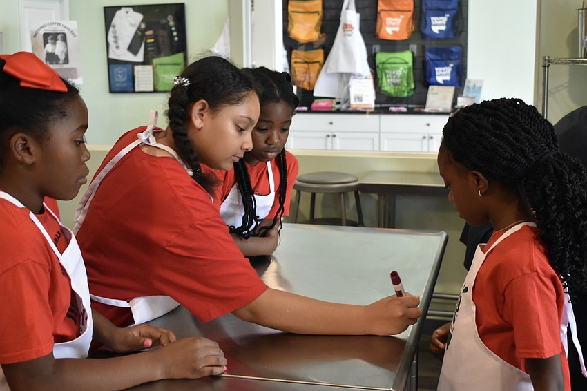 Mia, a third grader, Journee, a fifth grader, Jaleeyah, a sixth grader and Mahogany, a third grader, write their team name on their table.