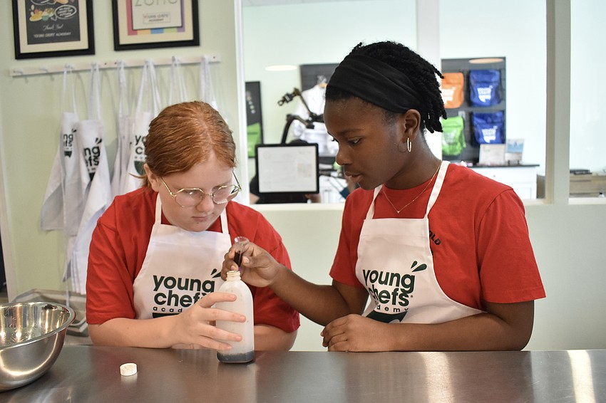 Sixth graders Meadow and Emma carefully measure out an ingredient.