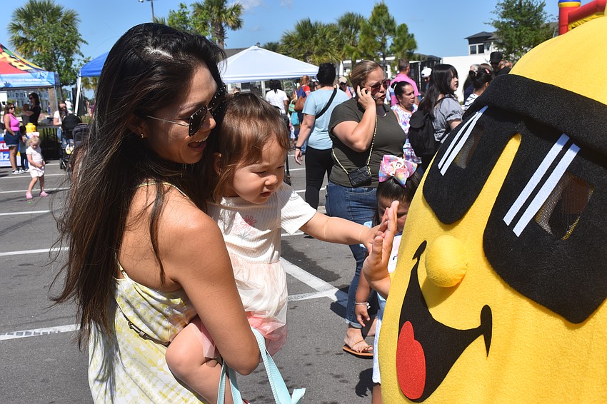Shirlene Kodiak holds her daughter Siena Kodiak so she can get up close with the mascot at the Sunshine Movers booth.