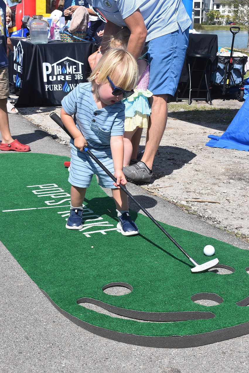 Jude Tomchinsky, 2, warms up for the egg hunt, by sinking some putts at the PopStroke booth.
