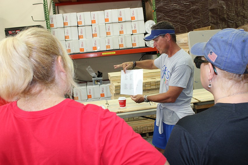 Todd Shear, a major in the Manatee County Sheriff's Office and a Beds for Kids board member, gives volunteers directions on painting Scripture verses on bed slats during the Keller Williams' Red Day.