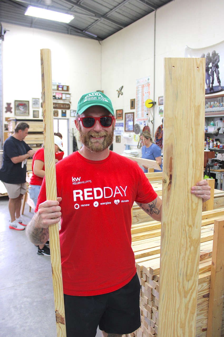 Brad Wollweber, who trains employees for Keller Williams, carries more lumber to the workers for the bed frames.
