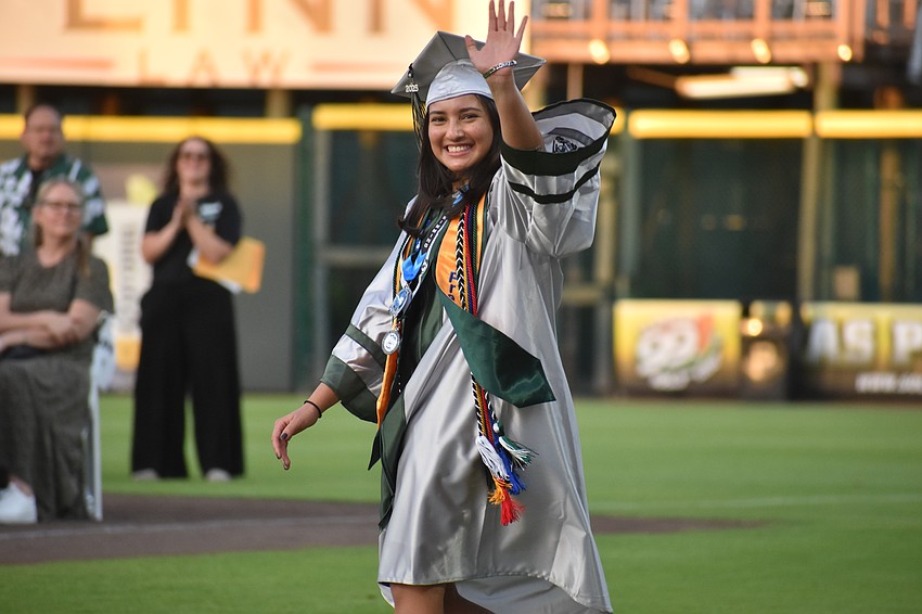 Commencement speaker Nadia Gandi makes her way to receive her diploma while waving to the crowd.