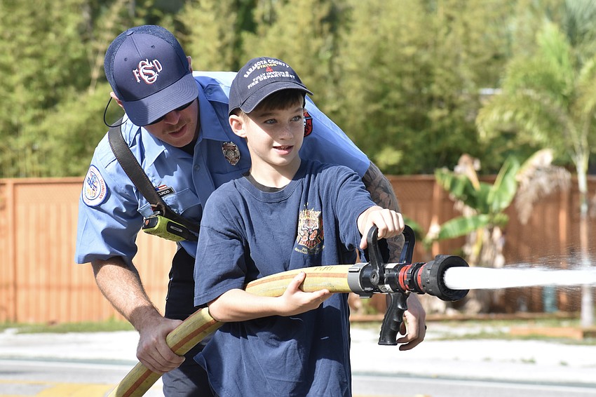 Tyler Curcio shows Mason Foscolos, 9, how to use the fire hose.