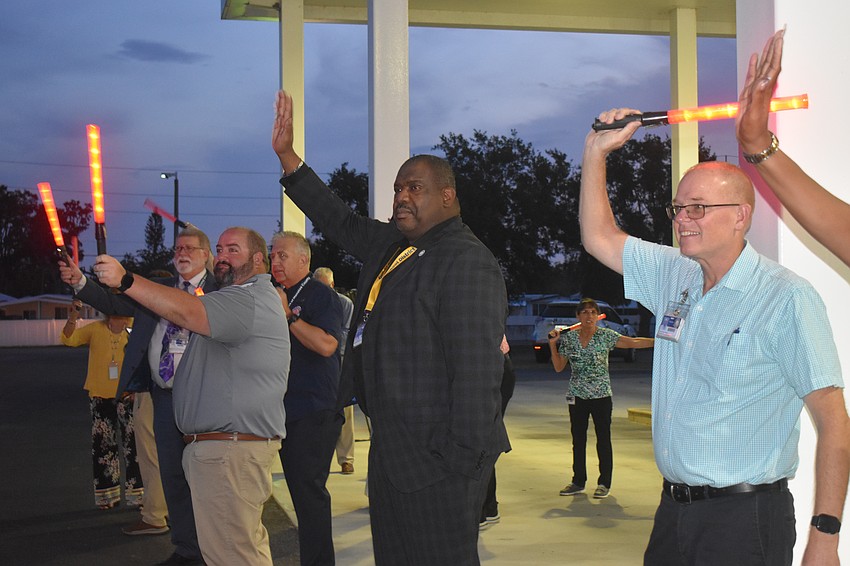 School board Member Chad Choate, Associate Director of Strategic Planning Omar Edwards, and Director of Transportation Jamie Warrington wave to bus drivers with glow sticks.