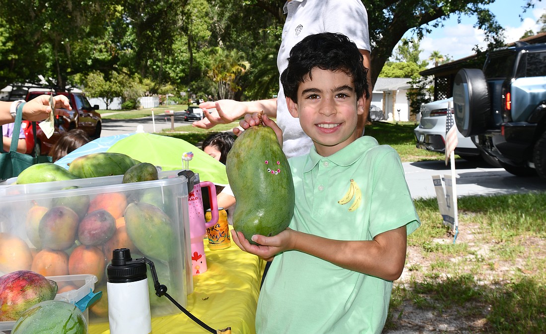 Aaron Briskman holding one of the biggest mangoes from his family’s mango tree with a smiley face.