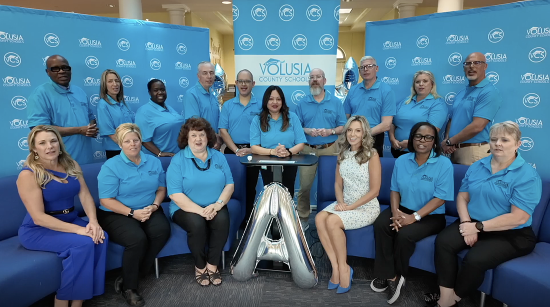 Volusia County Schools Superintendent Carmen Balgobin announces the district's "A" grade alongside district staff and School Board member Krista Goodrich (front, left), School Board Chair Jamie Haynes (front, third from left) and School Board member Jessie Thompson (front, third from right). Screenshot courtesy of VCS