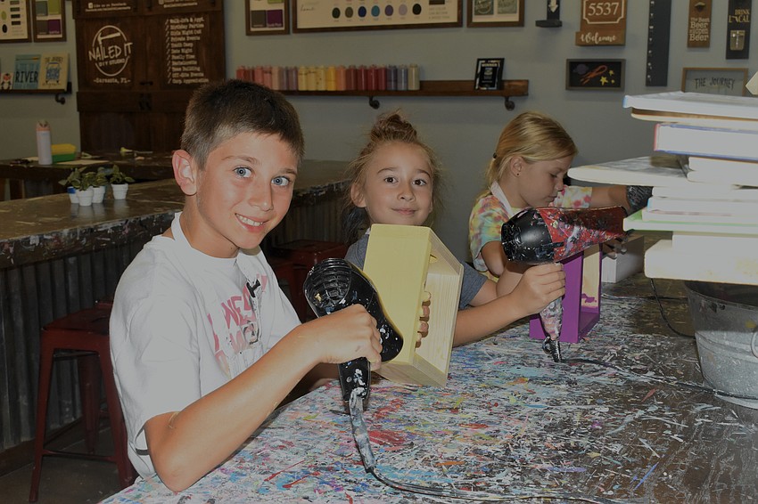 Chase Campbell, 8, Olivia Sarkisova, 8 and Abbie McCarthy, 7, dry the paint on their plant holders.