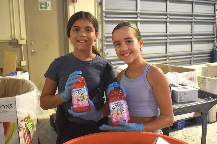 Sarasota resident Catalina Poole, 11 and Waterside resident Bianca Azevedo, 11, check the expiration of Hawaiian Punch containers. It was not expired so they relocate it to the beverages box.