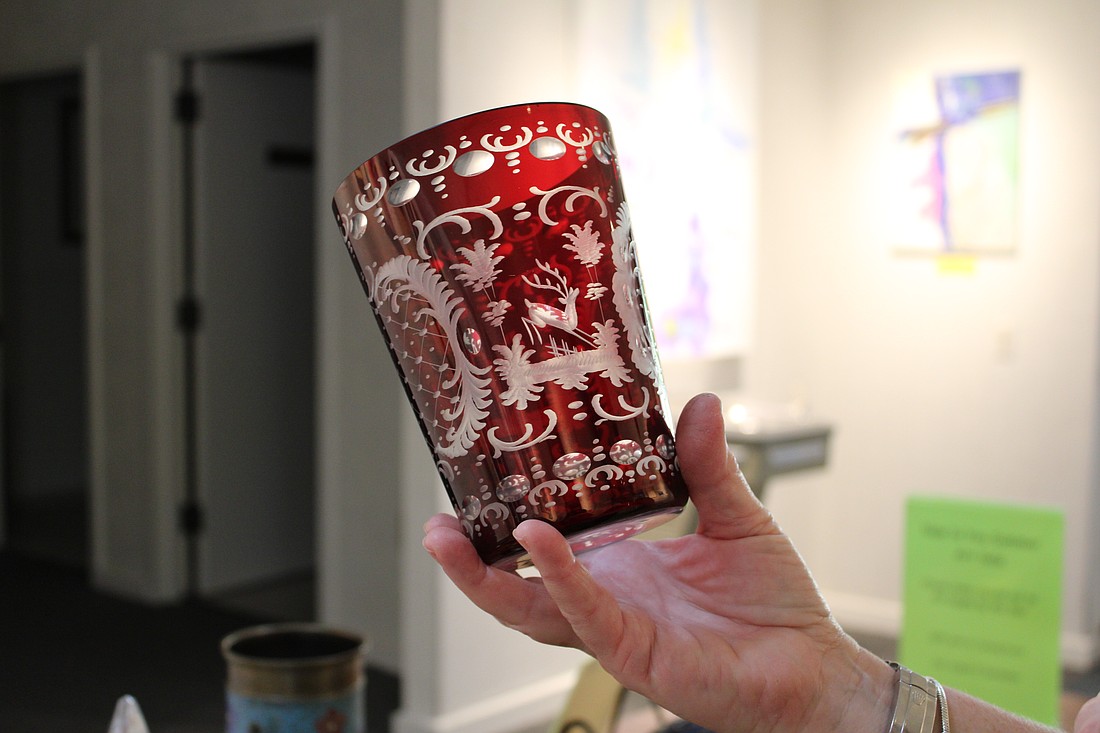 Linn Torres, All Angels by the Sea administrative assistant and art sale coordinator, holds up a decorative glass piece, one of the many art items for sale at this summer's New to You art sale at the church.
