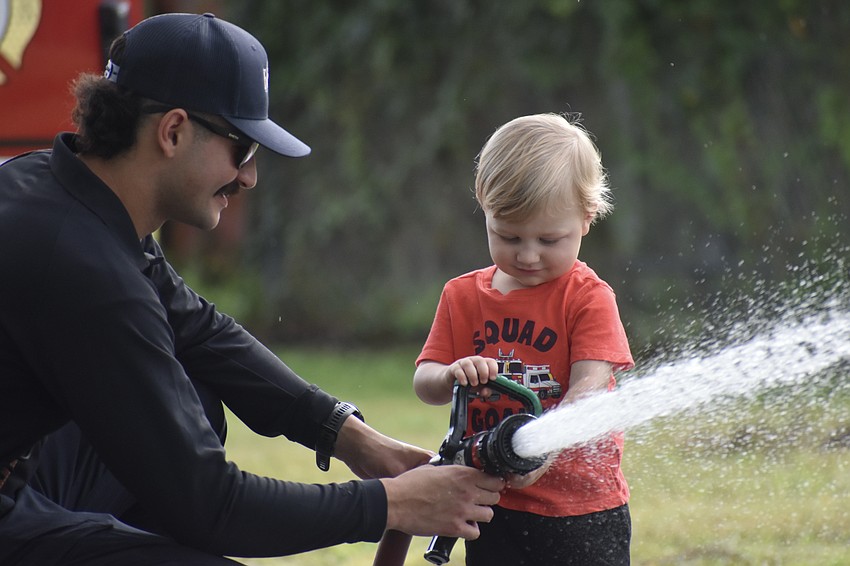Firefighter Goldwich Parker helps Dylan Slowik, 2, use the fire hose.