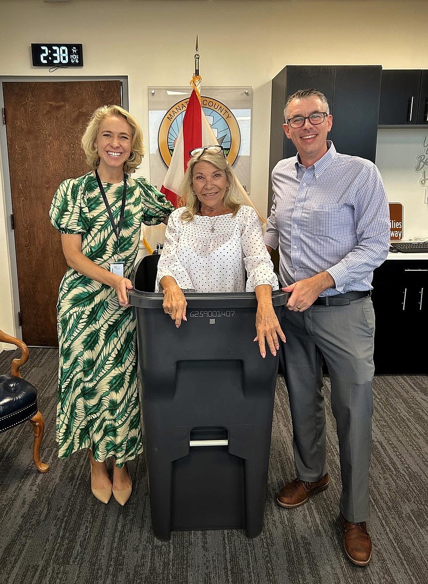 Commissioner Carol Felts illustrates the size of the 'big bins' by getting in one. From left to right: Director of Government Relations Stephanie Garrison, Felts and Communications Division Manager Casey Zempel.