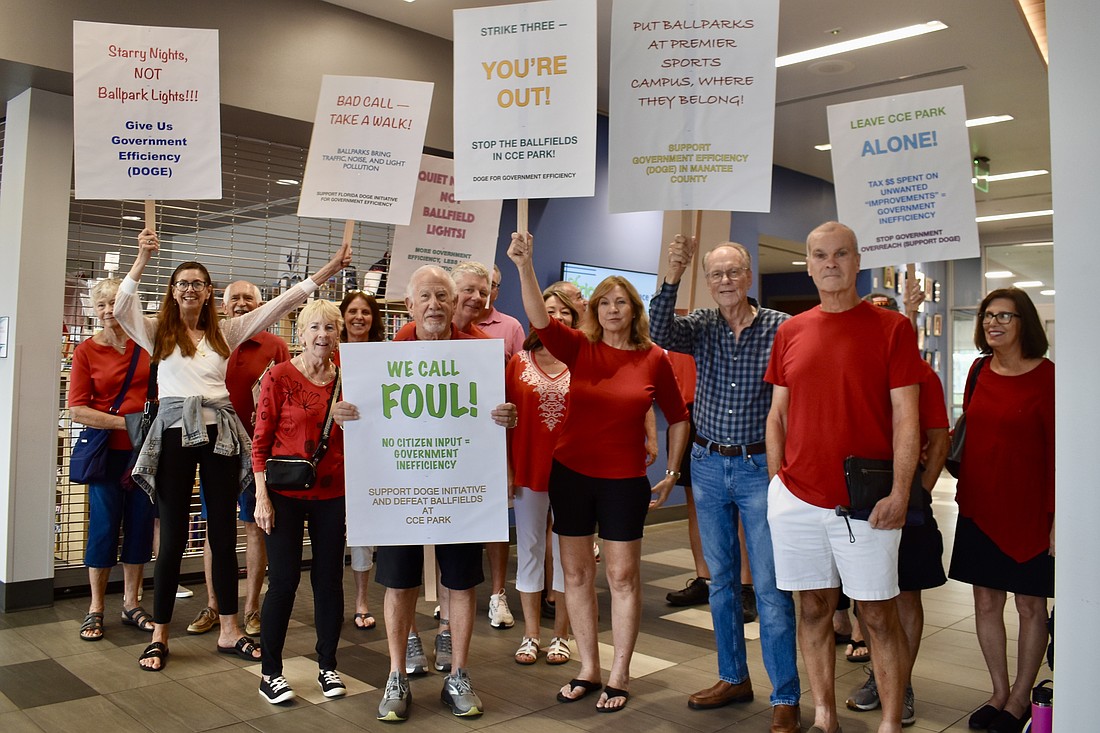 Rain drives the protest against the Little League fields inside the Lakewood Ranch Library for a photo, but library supervisor Tiffany Mautino wants it noted that protests are not allowed inside the library.