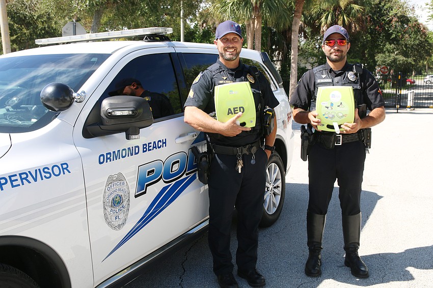 Ormond Beach Police Sgt. Caleb Braun and Officer Josh Morris hold the AEDs outside a patrol vehicle. Photo by Jarleene Almenas