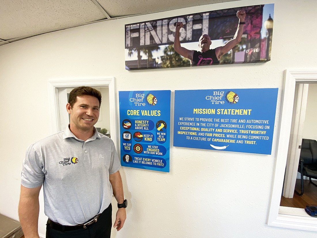 Reed Parman, president of Big Chief Tire, is the fourth generation of his family to lead the Jacksonville-based tire and auto servicing business. He stands beneath a photo of his father, Fritz III, who ran the business until his death in 2021. Fritz Parman III was a marathon runner, and Reed Parman says he posted the image in several places in the Big Chief offices as an inspiration to continue striving toward success.