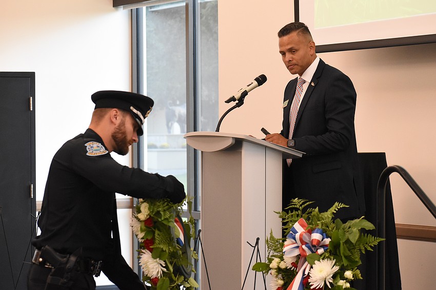 Officer Aaron Homan of the Sarasota Police Department lays a wreath as Carlos Moreira, Director for Campus Engagement for Veteran Success at USF Sarasota-Manatee stands at the podium.