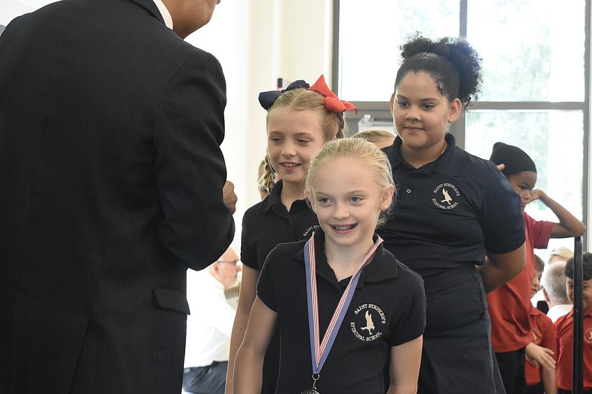 Carlos Moreira, Director for Campus Engagement for Veteran Success at USF Sarasota-Manatee, hands medals to Sabrina Davis, Natalie Andrade and Madeleine Dini of Saint Stephen's Episcopal School.