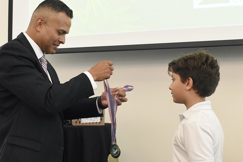 Carlos Moreira, Director for Campus Engagement for Veteran Success and Alumni Affairs at USF Sarasota-Manatee gives a medal to Julian Coles of Saint Stephen's Episcopal School.
