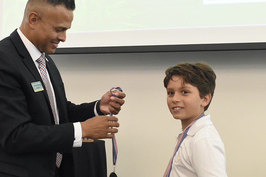 Carlos Moreira, Director for Campus Engagement for Veteran Success at USF Sarasota-Manatee gives a medal to Julian Coles of Saint Stephen's Episcopal School.