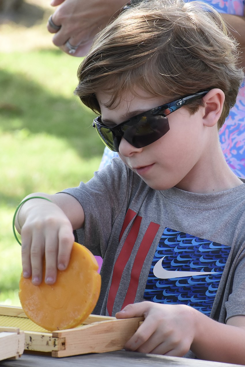Rylan Albright, 7, rubs beeswax onto a frame.