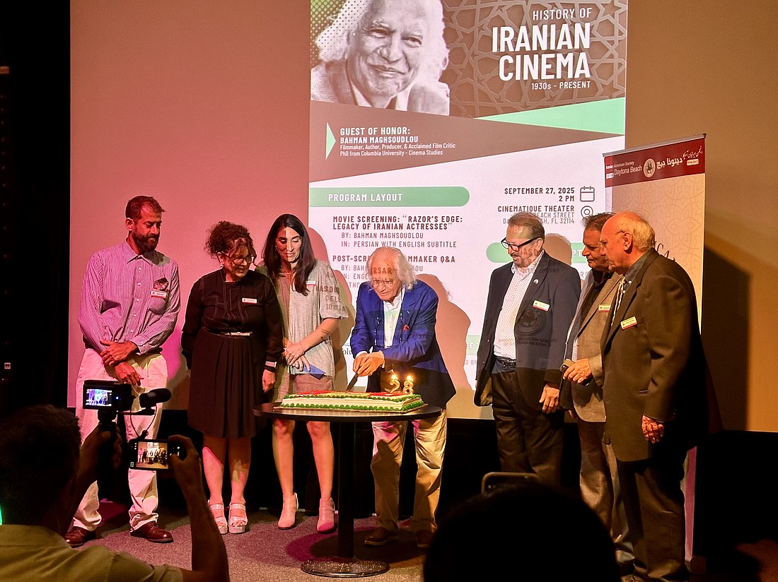 Filmmaker Bahman Maghsoudlo (center) cuts the first slice of the Iranian American Society of Daytona Beach's 28th anniversary cake on Sept. 27. Courtesy photo
