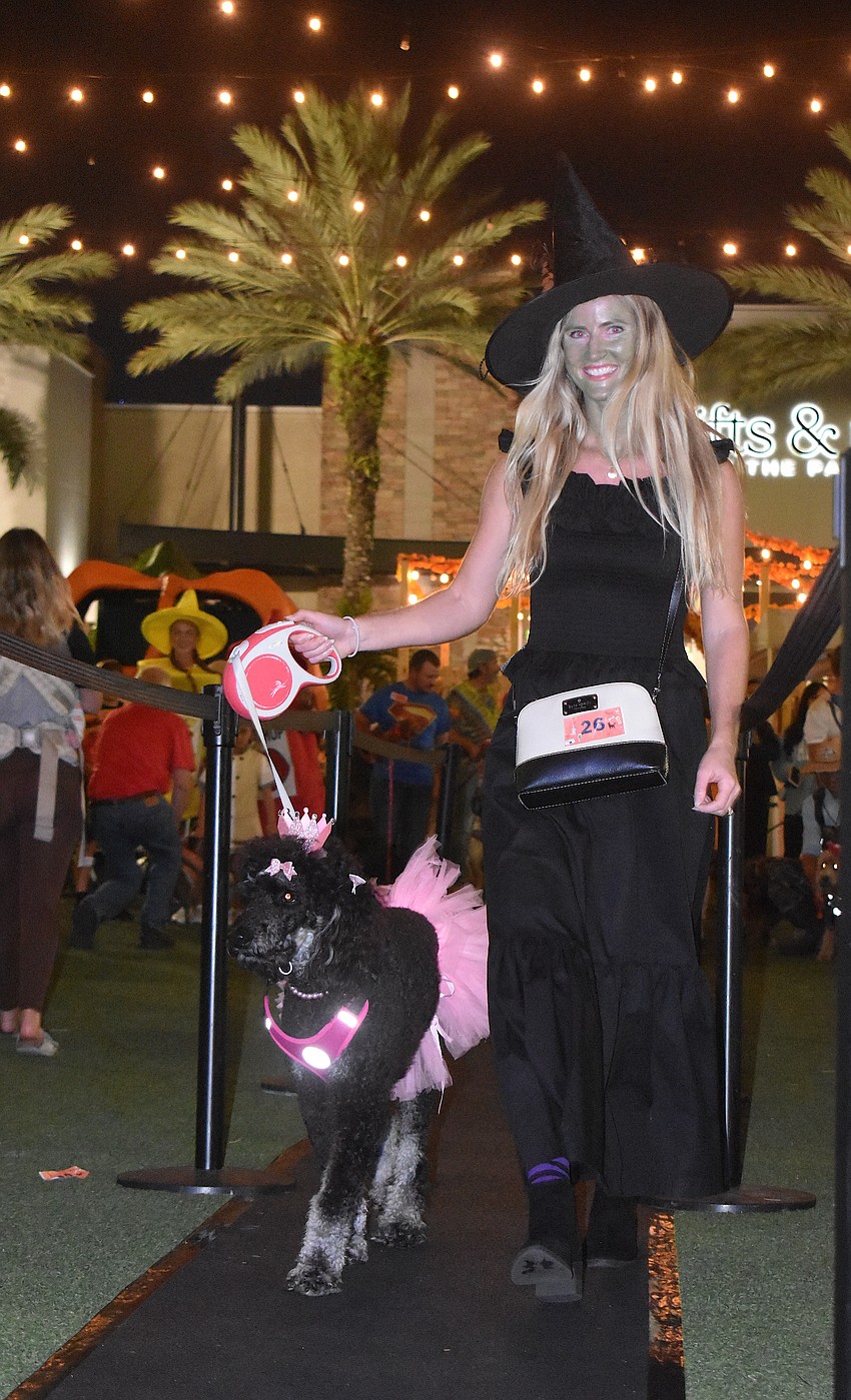 Rye, a 2-year-old poodle dressed as Glinda the Good, walks with Eryn Skage who is dressed as the Wicked Witch of the West.