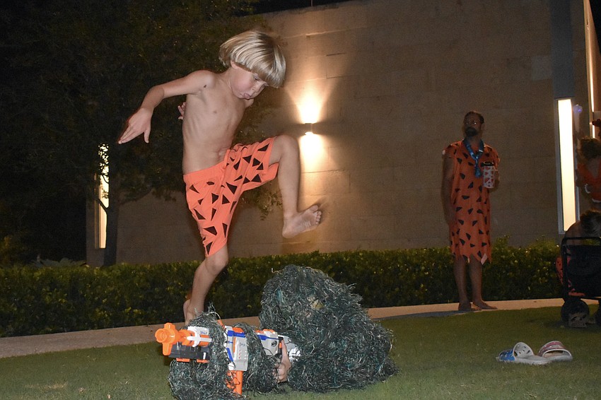 With the energy of Bamm-Bamm Rubble, Sequoia Kemper, 6, jumps over his brother Bowen Kemper, 11, who is performing an operation with a Nerf gun in the park grass. Their father Kyle Kemper stands behind them.