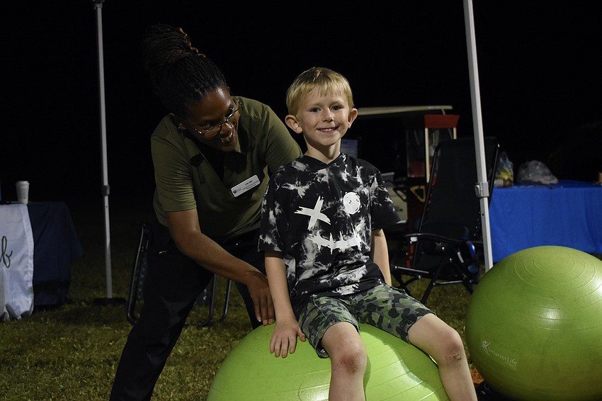 Halima Anderson of Capacity Faith Relief helps Matthew Servetz, 7, atop an exercise ball.