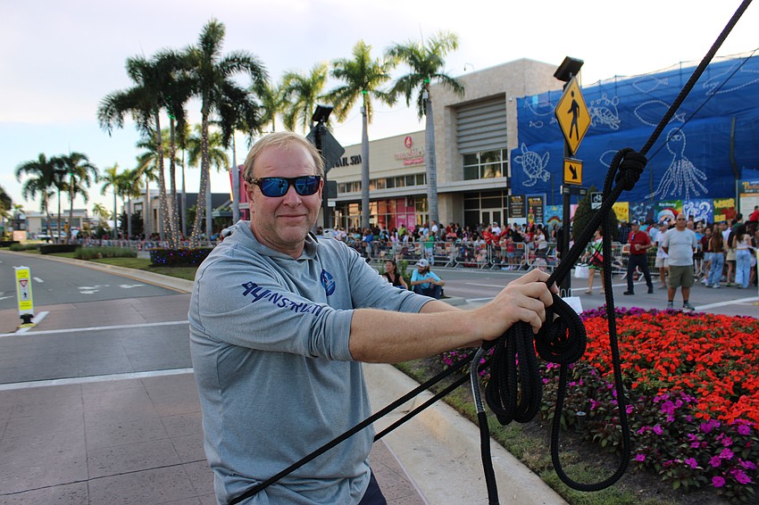 Paul Voloshen volunteers to hold one of the many ropes that keep the wires tight for the criss-cross skywalk attempt by Nik Wallenda and his sister Lijana Wallenda at the Santa's Grand Arrival Parade.