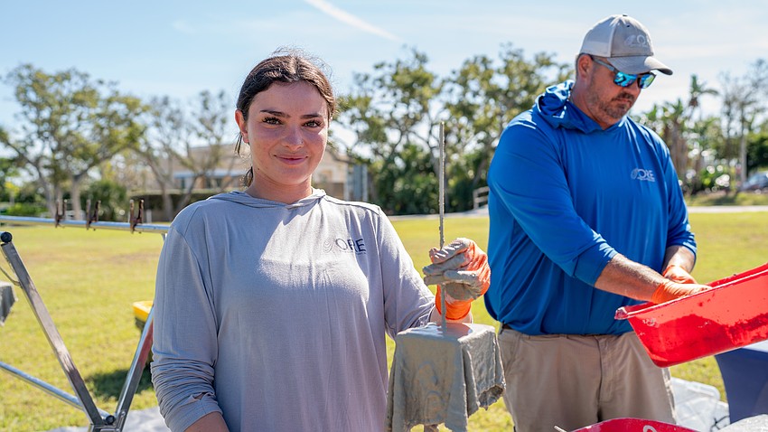 Oyster River Ecology ecological restoration technician Abbey Kuhn poses for a photo with an oyster rag pot she made at the Rotary Club of Longboat Key’s Food for Gratitude event where all town employees received free lunch to recognize their hard work after dual hurricanes in 2024. To the right, ORE founder and executive director Damon Moore mixes up some concrete.