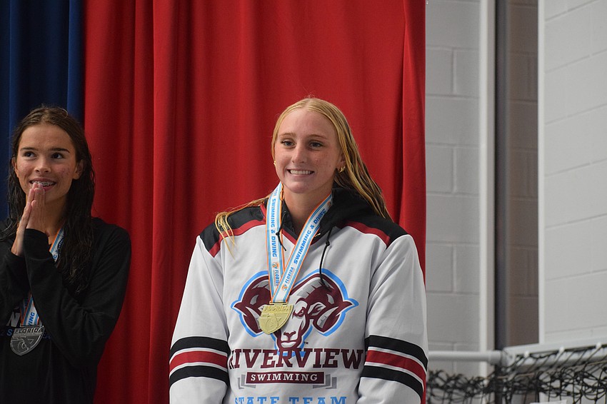 Senior Taylor Schwenk smiles for a photo with her gold medal after winning the 100-yard butterfly. Her three first-place finishes were the most of any Ram at the state meet.