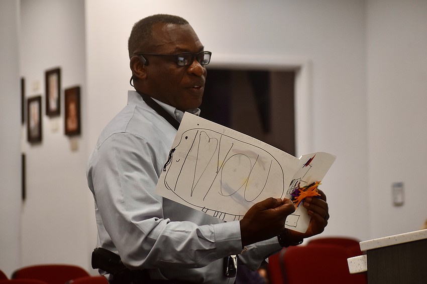 Deputy John Murrell holds up pictures, one of which was drawn by a child who feared police, to illustrate the positives that can come from law enforcement engaging with youths.