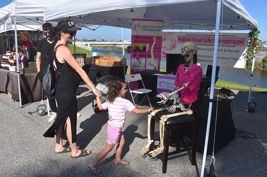 Sarasota's Jordan Reynolds provides support to 4-year-old daughter Dela as she greets an animatronic skeleton, that moves and talks to customers, at the Adjust Your Life Chiropractic booth.