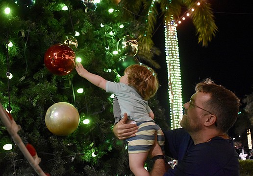 Sarasota's David Farr picks up 21-month-old Henry Farr, who is dazzled by the giant ornaments on the tree on The Green during the Mall at UTC's ongoing holiday celebration.