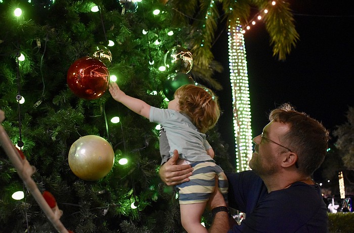 Sarasota's David Farr picks up 21-month-old Henry Farr, who is dazzled by the giant ornaments on the tree on The Green during the Mall at UTC's ongoing holiday celebration.
