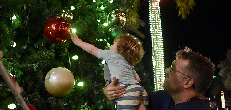 Sarasota's David Farr picks up 21-month-old Henry Farr, who is dazzled by the giant ornaments on the tree on The Green during the Mall at UTC's ongoing holiday celebration.