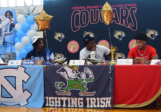 Kymistrii Young (left), Elijah Golden (center) and Macaiden Brown (right) listen to coach Jared Clark's speech during Cardinal Mooney's early signing period ceremony.