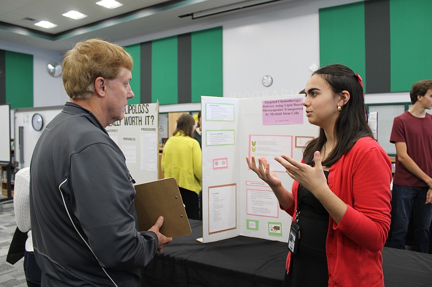 Bryan Thomas, a science teacher and judge at the fair, listens as senior Addison Wiele discusses her project on targeted chemotherapy.
