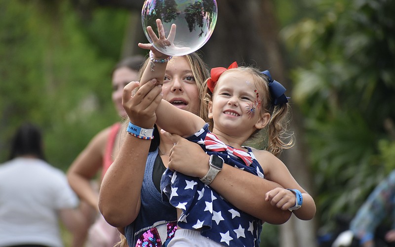 Gabriella Brinceanu, 14, and her sister, Alaina Brinceanu, 3, work together to pop the bubbles at the Fourth of July All-American Cookout at Marie Selby Botanical Gardens. Attendees enjoyed the bubble show by Blaise Ryndes, who has appeared on “America’s Got Talent.”