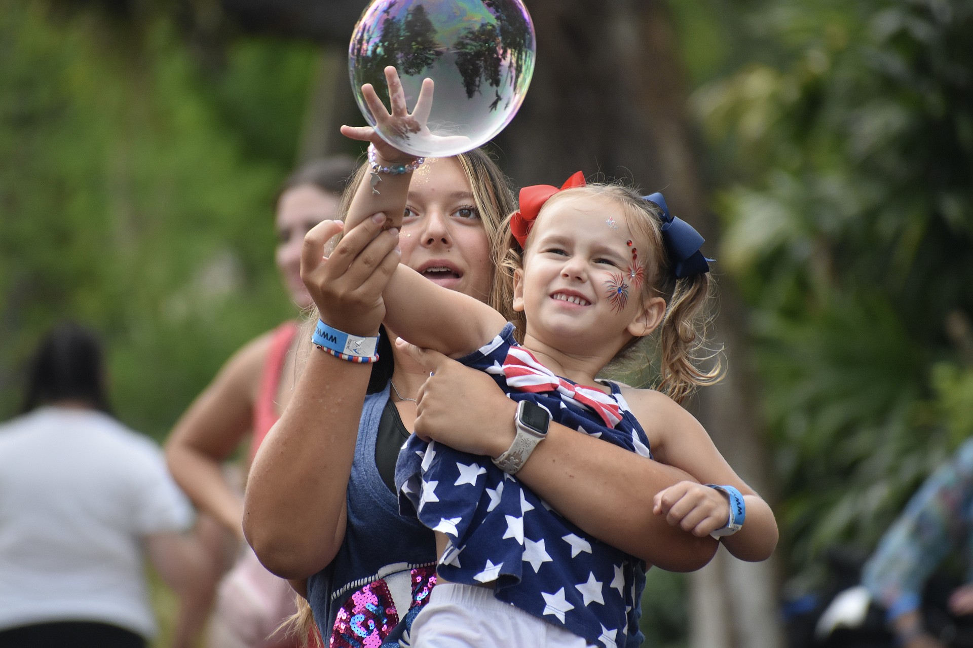 Gabriella Brinceanu, 14, and her sister, Alaina Brinceanu, 3, work together to pop the bubbles at the Fourth of July All-American Cookout at Marie Selby Botanical Gardens. Attendees enjoyed the bubble show by Blaise Ryndes, who has appeared on “America’s Got Talent.”