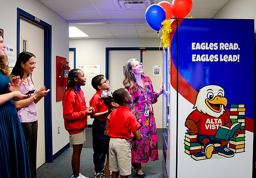 Bonnie Michaels, literacy coach at Alta Vista Elementary School, helps students Deja (5th grade), Gianni (4th grade), Yoselyn (1st grade) and Andre (2nd grade) try out the new book vending machine. Sarasota Yacht Club youth board members coordinated the installation to help promote strong reading habits.