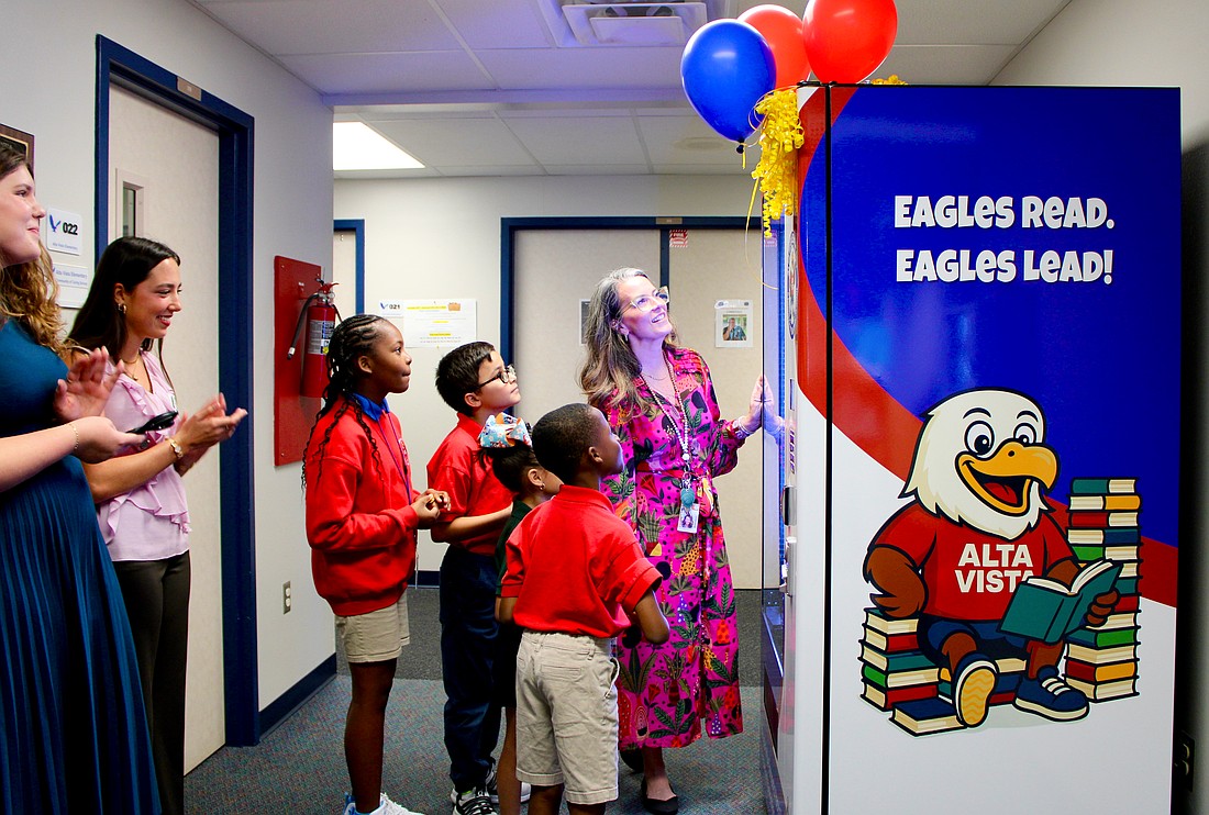 Bonnie Michaels, literacy coach at Alta Vista Elementary School, helps students Deja (5th grade), Gianni (4th grade), Yoselyn (1st grade) and Andre (2nd grade) try out the new book vending machine. Sarasota Yacht Club youth board members coordinated the installation to help promote strong reading habits.